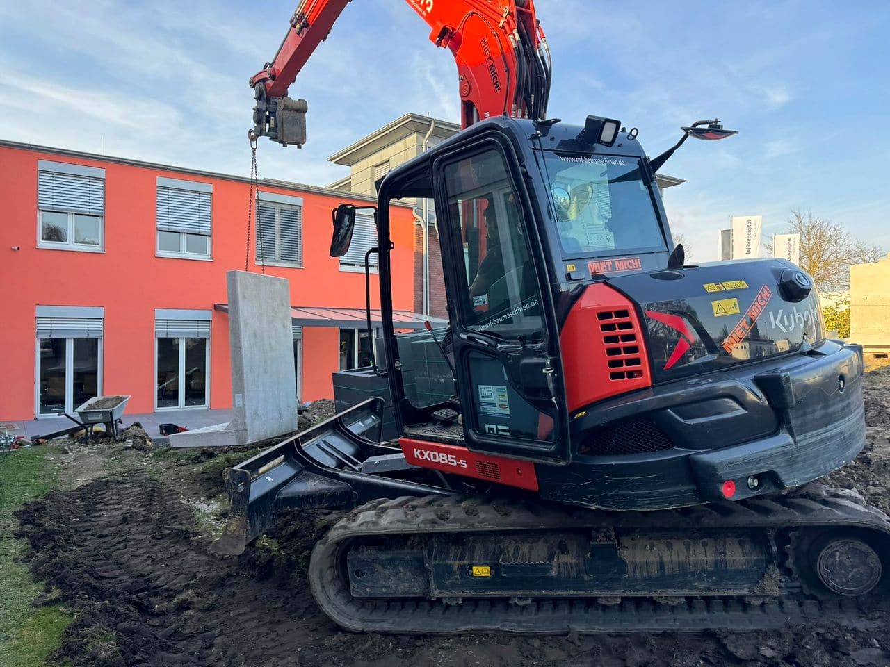 Ein großer L-Stein hängt an Ketten am Bagger und wird vor dem Haus in Position gebracht