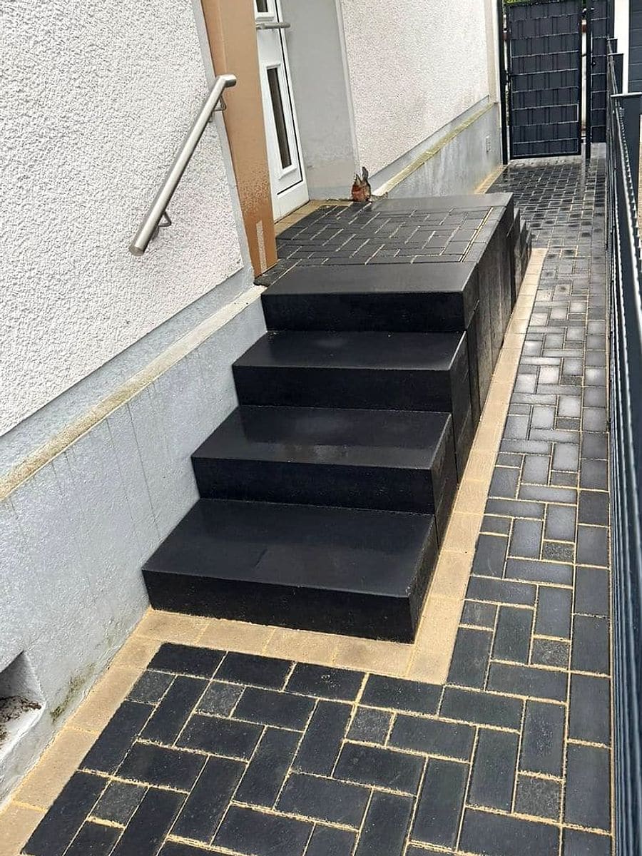 Nachher: Treppe aus anthrazitfarbenen Blockstufen mit gepflastertem Podest, heller Randstreifen und Weg im Fischgrätverband