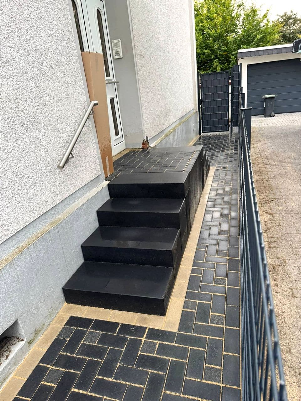 Neue Treppe aus anthrazitfarbenen Blockstufen am Hauseingang mit Pflasterweg im Fischgrätverband