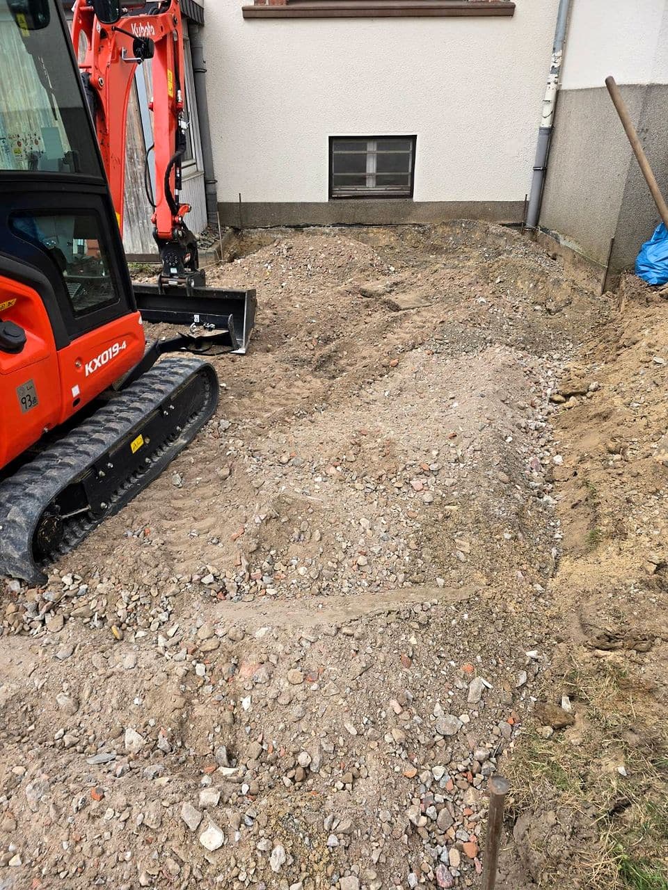 Ausgehobene Fläche bis an die Hauswand, daneben der Minibagger
