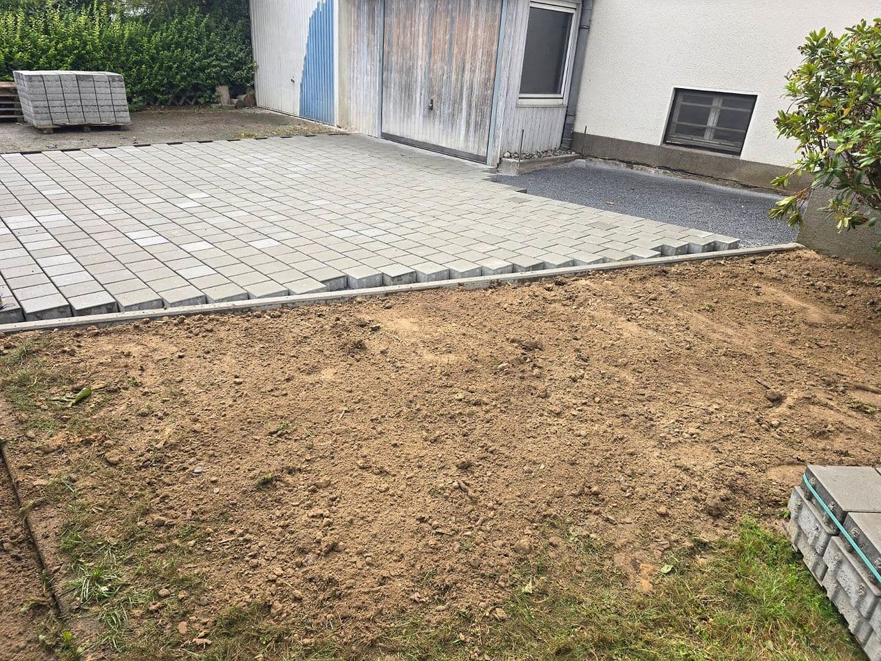 Pflaster während der Verlegung, davor die für neuen Rasen vorbereitete Fläche