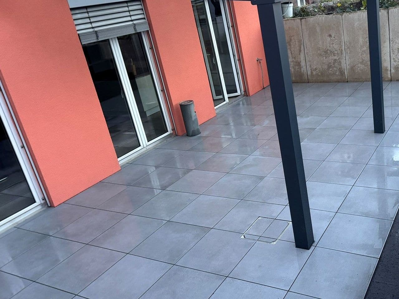 Nachher: fertige Terrasse aus großformatigen grauen Platten vor dem Haus in Bielefeld, hinten die L-Stein-Wand